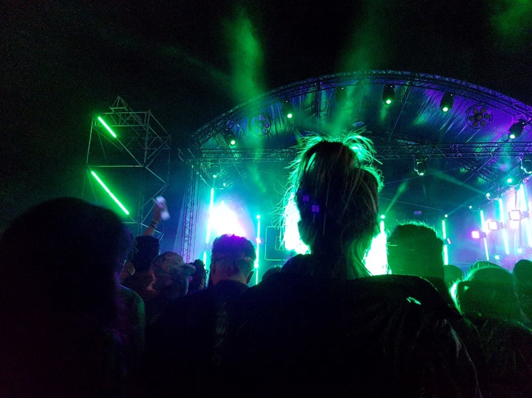 A young woman from the back dances standing in front of the stage among the crowd of festival goers. Photograph by Amaury Cornu / Hans Lucas.