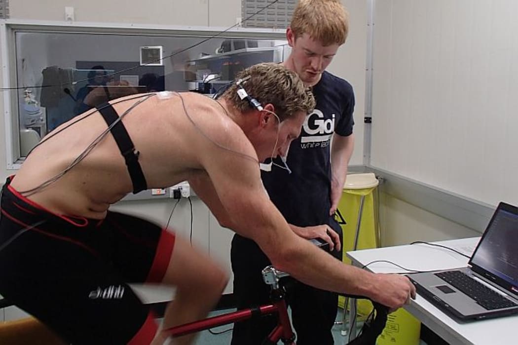 PhD student Ashley Akerman (standing) supervises triathlete Rob Creasy who is undertaking a strenuous work-out on an exercycle in a room heated to 40 degrees Celsius with 60% humidity.