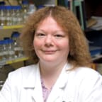 Dr Primrose Freestone - a redheaded woman in a white coat - smiles slightly at the camera.