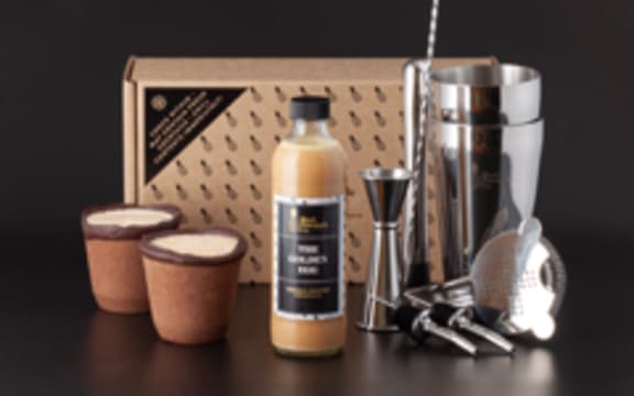 Image of a Golden Egg cocktail kit, featuring (left to right): two edible chocolate cookie cups, a bottle of mixed cocktail, various silver cocktail implements including a cocktail shaker