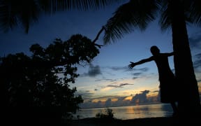 A child on Kiribati watches the sunset on an ever rising ocean.