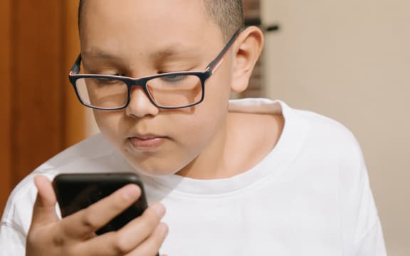 A teenage boy in glasses looks at phone