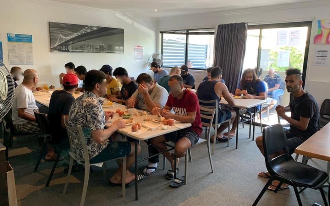 Hakeem Kakar (right) watches refugees eating their lunch in Brisbane.