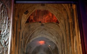 Stone vaults inside Notre-Dame Cathedral with flames are seen through the damaged roof.