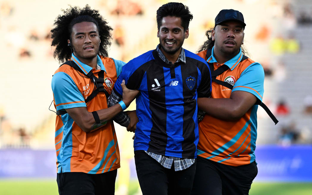 Security remove a pitch invader in an Auckland FC shirt from the field during the Wellington Phoenix v Sydney FC. A-League football match at Eden Park in 2024.