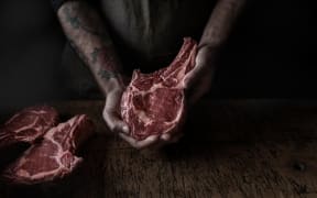 A person's arms with tattoos are seen holding raw beef.