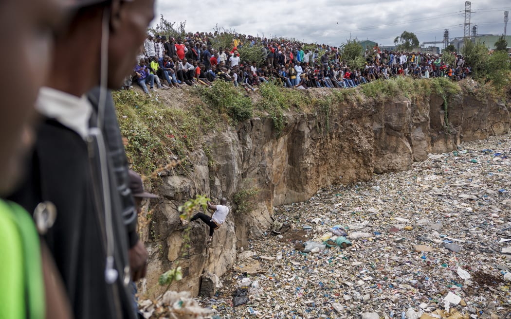 Crowds gather on the edge of an abandoned quarry to watch volunteers searching through a rubbish dump for human remains at Mukuru slum in Nairobi on July 14, 2024. Eight female bodies have been recovered so far from a dumpsite in a Nairobi slum. The mutilated and dismembered bodies, trussed up in plastic bags, were hauled out of a sea of floating rubbish in the abandoned quarry. Police chiefs said they were pursuing possible links to cults, serial killers or rogue medical practitioners in their investigation into the macabre saga, which has horrified and angered the nation. (Photo by Tony KARUMBA / AFP)