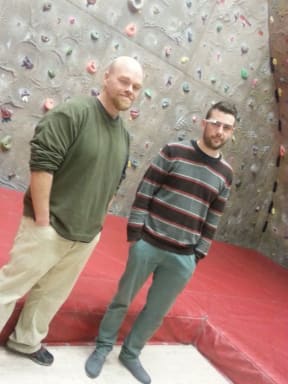 A photo of Deak Helton standing in front of the climbing wall, with Alex Woodham wearing Google Glass