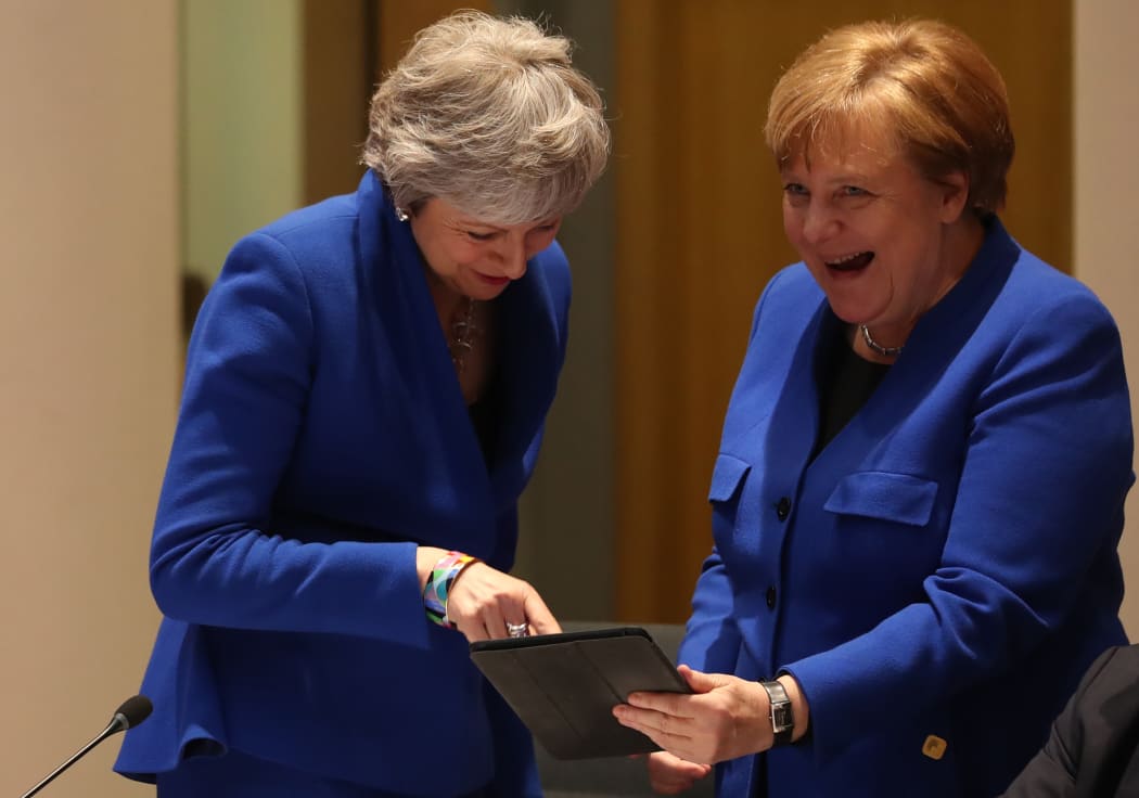 Theresa May and Angela Merkel share a laugh over something on a tablet during the crunch summit in Brussels.