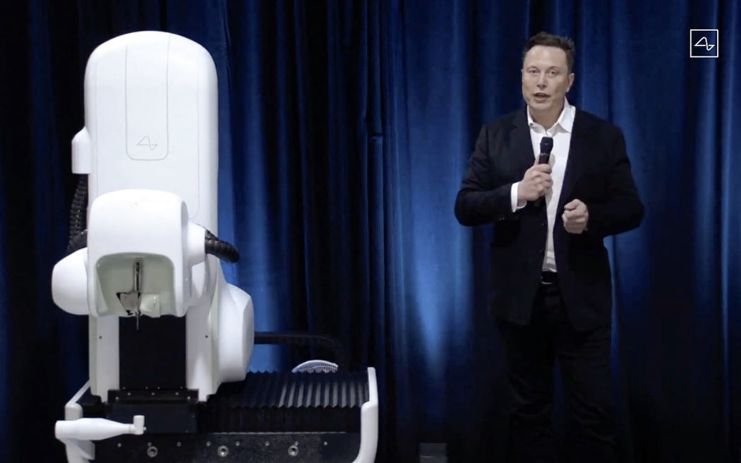 This video grab from the online Neuralink livestream shows Elon Musk standing next to a surgical robot during his Neuralink presentation on August 28, 2020.