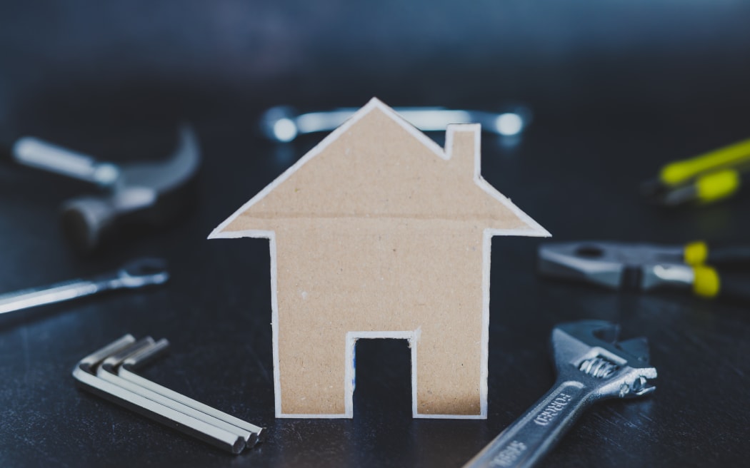 do it yourself and home renovation concept: little house made of cardboard and DIY tools in the background shot at shallow depth of field
