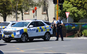 Lights are out at Birkenhead Ave intersection with Onewa Road and traffic is being manually directed by a person in a high-vis vest while armed police guard a cordon.