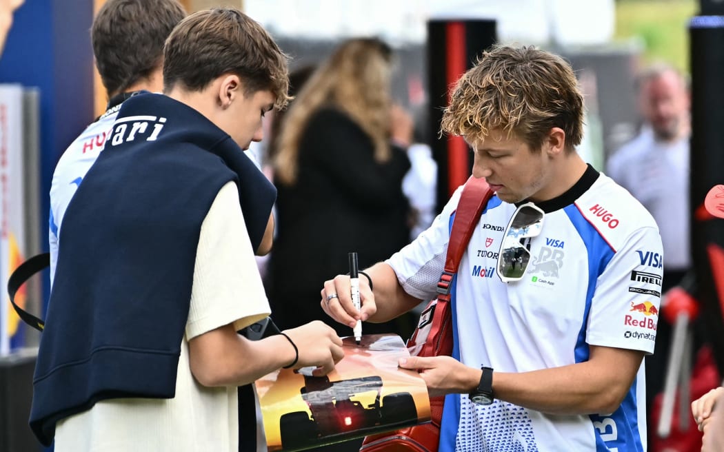 Racing Bulls' New Zealand driver Liam Lawson (R) signs an autograph for a fan as he arrives ahead of the third practice session at the Red Bull Ring race track in Spielberg, Austria, on June 28, 2025, ahead of the Formula One Austrian Grand Prix. (Photo by Joe Klamar / AFP)