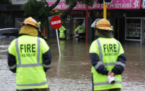 Firefighters check shops for people trapped in floodwaters in the west Auckland suburb of New Lynn.