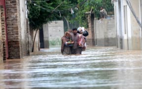 PESHAWAR, PAKISTAN - AUGUST 27: Displaced people wade through a flooded area in Peshawar, Khyber Pakhtunkhwa, Pakistan on August 27, 2022. Since June, nearly 900 people have died by severe monsoon rains and floods in Pakistan, while thousands have been displaced and millions more affected. Thousands of people who live in areas under threat of flooding have been told to evacuate. Hussain Ali / Anadolu Agency (Photo by Hussain Ali / ANADOLU AGENCY / Anadolu Agency via AFP)