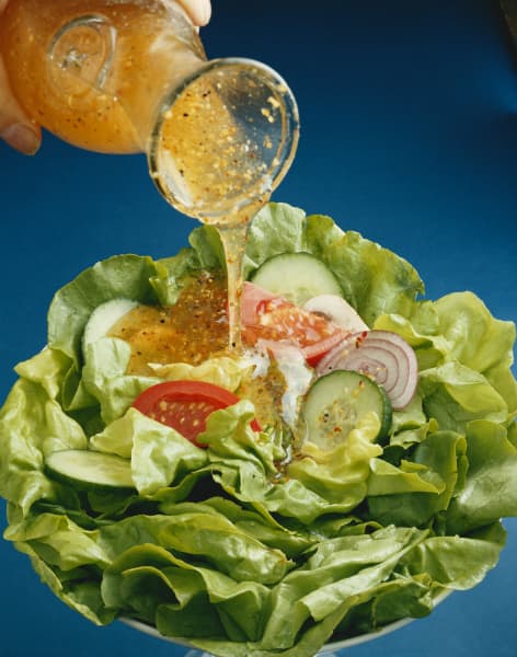 A person pouring a salad dressing on a leafy green salad.