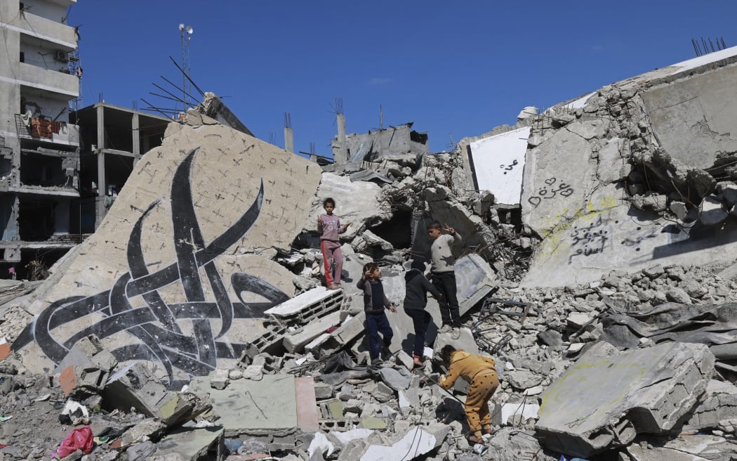 Children stand next to a fallen wall bearing a mural painting amid the rubble of a building destroyed in Israeli bombardment in Rafah in the southern Gaza Strip on February 22, 2024, amid continuing battles between Israel and the Palestinian militant group Hamas. (Photo by MOHAMMED ABED / AFP)