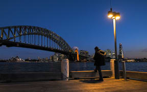 A man stands under a light in front of the Sydney Harbour Bridge at Milson's Point, during lockdown in Sydney.