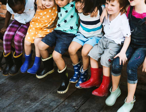 Children sitting in a row with arms around each other, smiling and wearing gumboots.