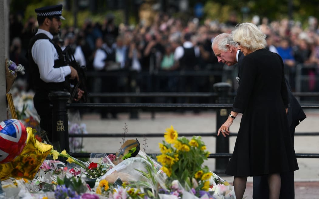 Britain's King Charles III (L) and Britain's Camilla, Queen Consort look at flowers and tributes as they greet the crowd upon their arrival Buckingham Palace in London, a day after Queen Elizabeth II died.