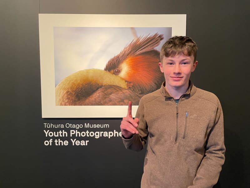 Monty McGee standing by his photo of a native crested grebe. The photo is called Pūteketeke Yoga.