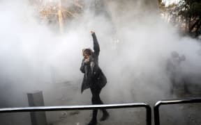 An Iranian woman raises her fist amid the smoke of tear gas at the University of Tehran during a protest driven by anger over economic problems, in the capital Tehran.