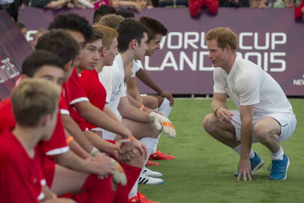 Prince Harry crouches for a chat with his team during the match.
