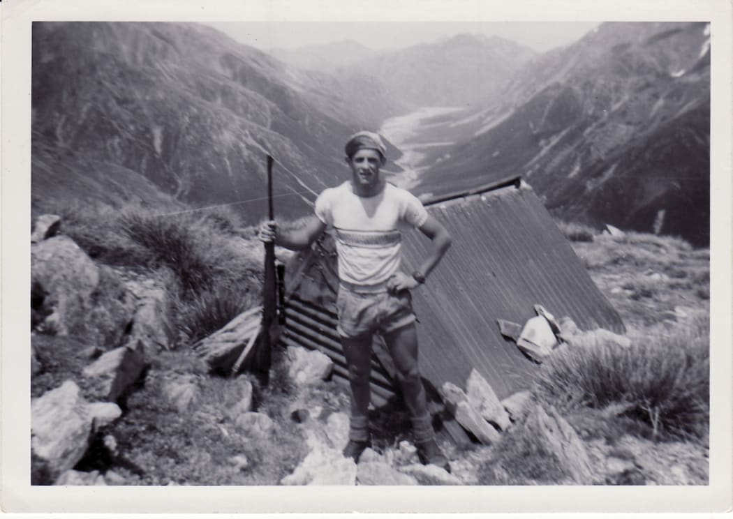 Man with gun outside of hut