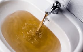 Dirty brown water running into a white sink. Looks very unhealthy,