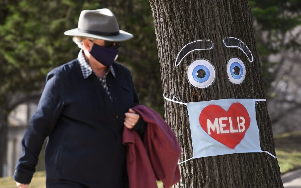 A man walks past a large face mask pinned to a tree in Melbourne on August 3, 2020 after the state announced new restrictions as the city battles fresh outbreaks of the COVID-19 coronavirus. -