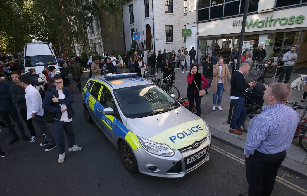 People stand in the street by a Police car close to Parsons Green underground tube station.