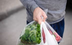 Man carrying plastic bag in his hand after shopping. Closeup of bag full of fruits and vegetables.