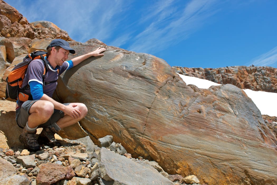 Glaciologist Shaun Eaves looks at glacial striations on a large rock above Whakapapa skifield. The scratches were made by a former glacier.