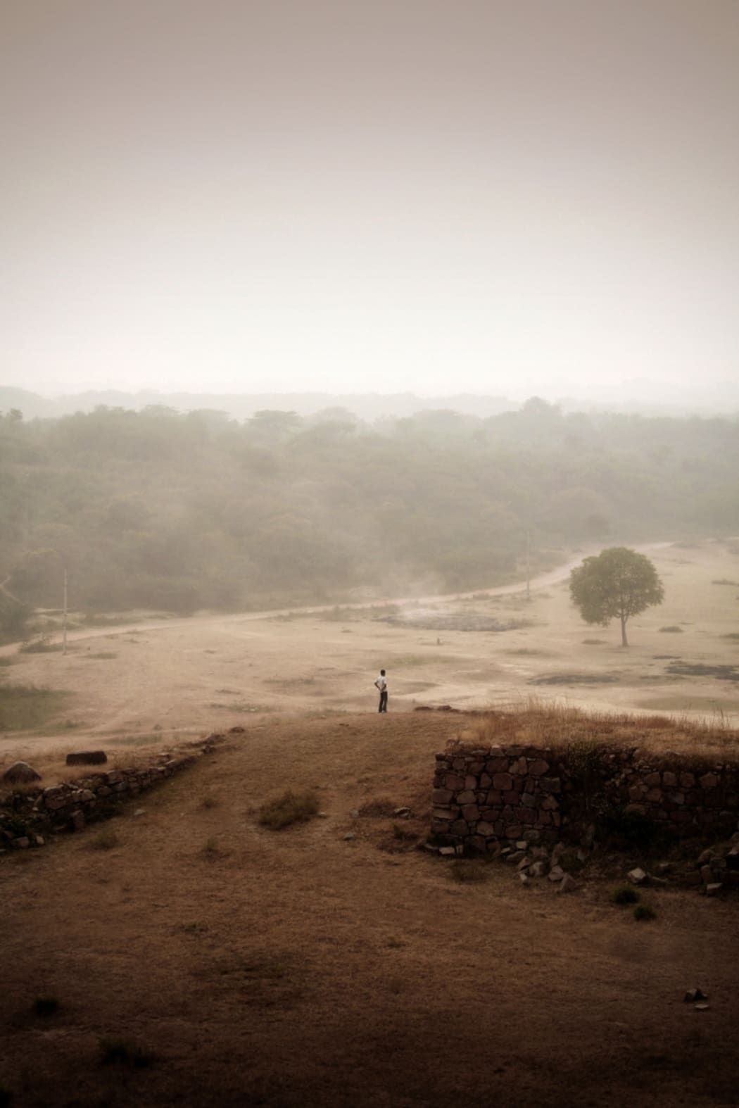 a lone man standing on a hill amongst smog in India