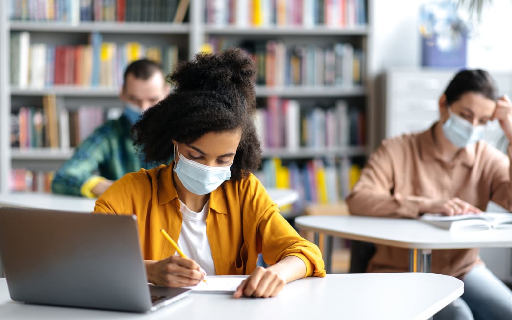 University students taking notes during lecture, wearing masks.