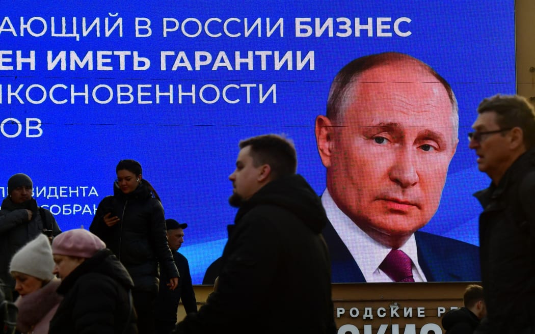 People pass by a digital screen displaying an image of Russian President Vladimir Putin and a quote from his recent address to the Federal Assembly, in Saint Petersburg on March 14, 2024.