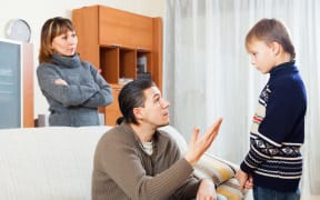 A photo of serious parents berating their teenage son at home
