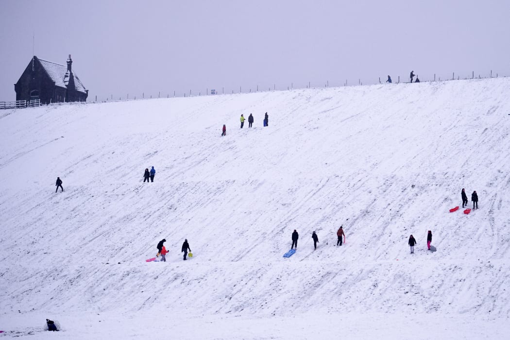 People sledge down a hillside at  Butterley Reservoir in Marsden, northern England on January 14, 2021 as heavy snow fell on parts of the UK