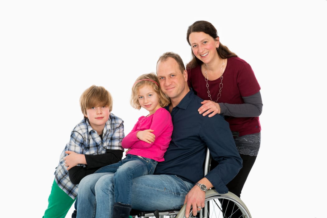 A photo of a disabled man in wheelchair with his family in front of white background