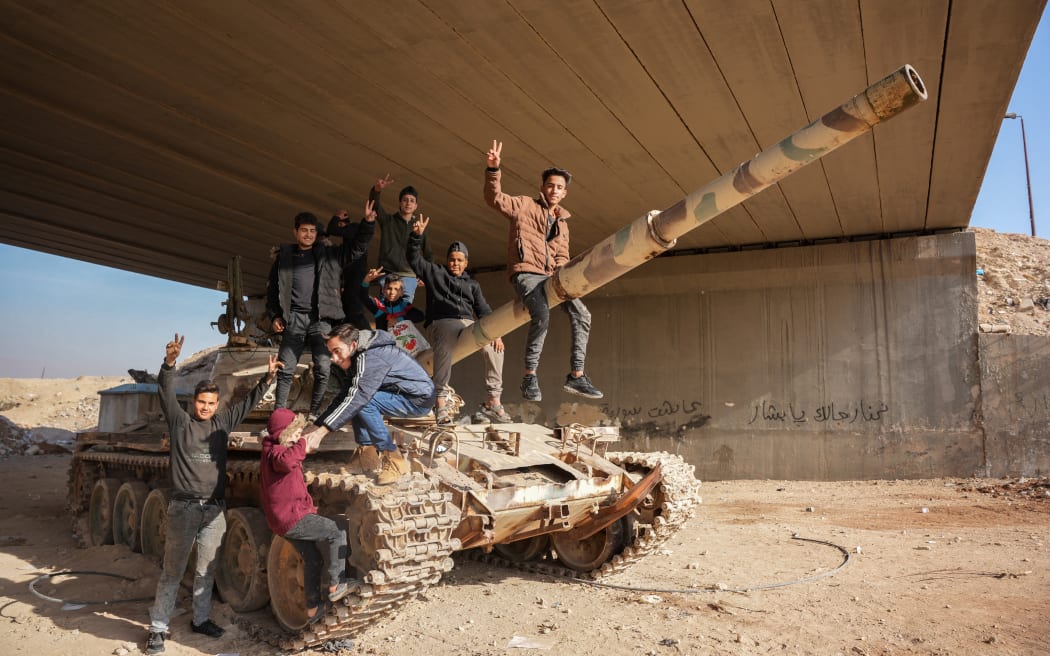 Syrians sit on an abandoned government tank in front of a slogan that reads 