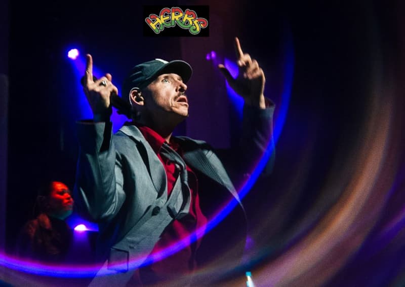 Tom Scott raises his forefingers in the air where the logo for the band Herbs has been placed.