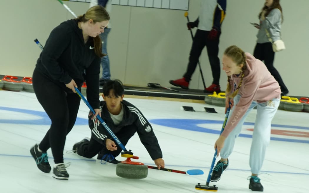 Picture depicts three young people engaged in the sport curling.