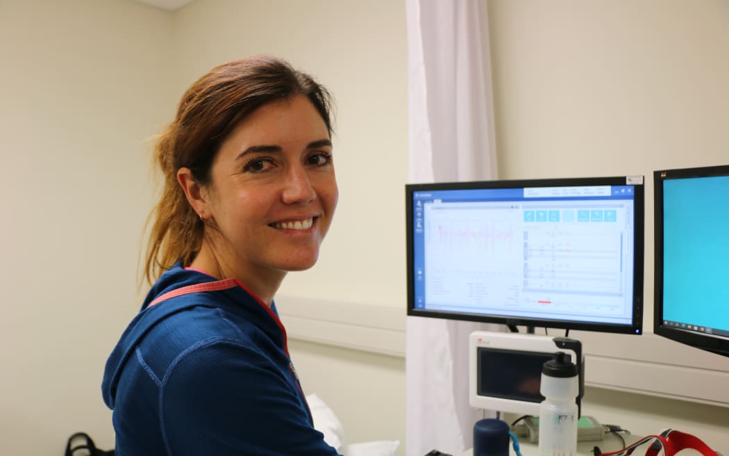 A woman sitting at a computer monitor turns to smile at the camera.