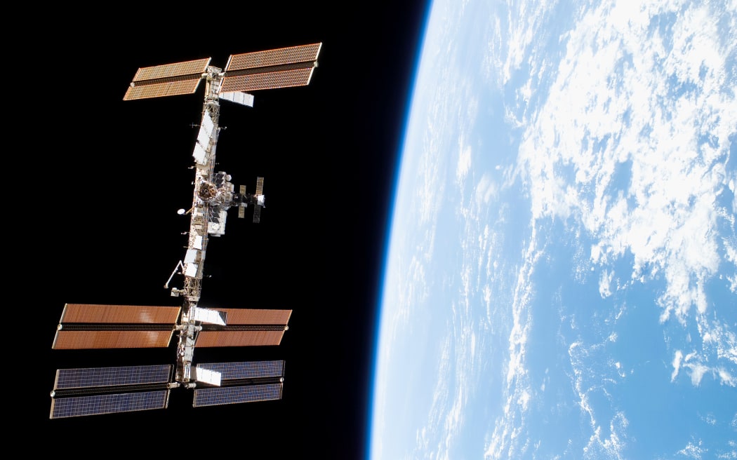 The International Space Station floats against the black backdrop of space adjacent to the glowing blue-and-white surface of Earth.