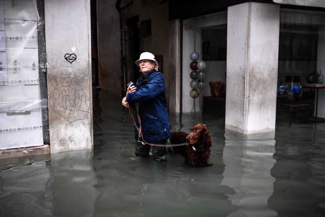 A woman walks her dog through a flooded street after an exceptional overnight "Alta Acqua" high tide water level, on 13 November, 2019 in Venice.