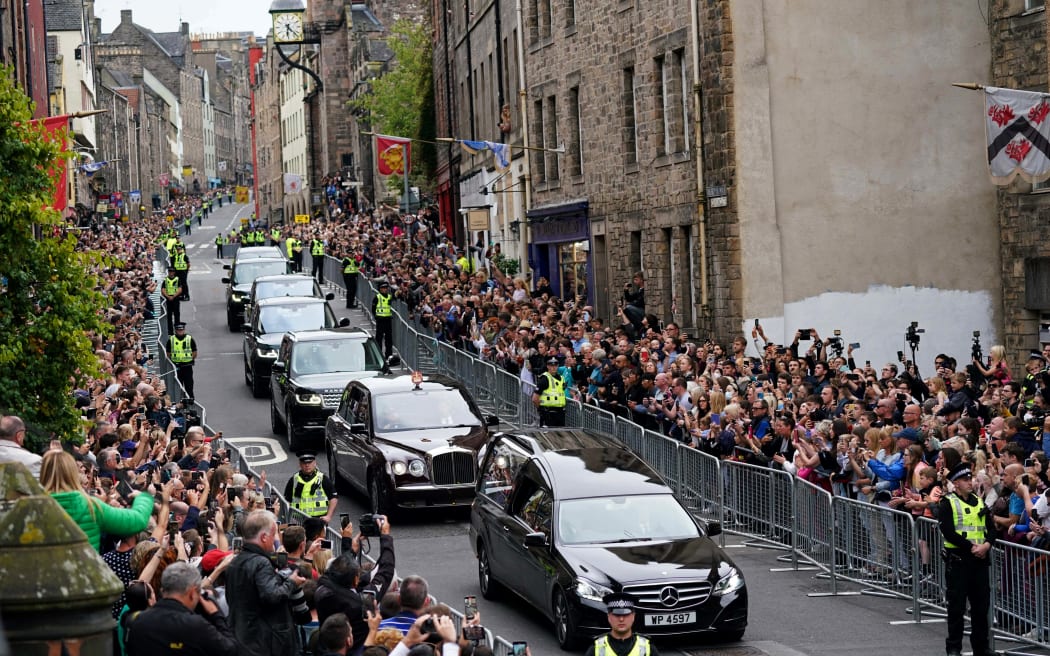 Members of the public stand on Cannongate to watch the hearse carrying the coffin of Queen Elizabeth II, draped in the Royal Standard of Scotland, as it is driven through Edinburgh towards the Palace of Holyroodhouse, on September 11, 2022.