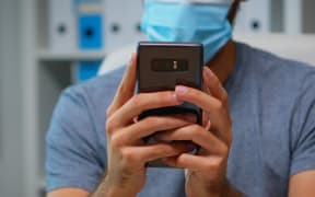 Close up of man with face mask typing text messages on smartphone sitting in workplace during coronavirus.