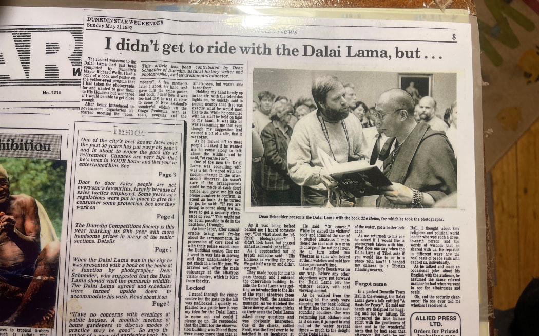 A newspaper clipping with the headline "I DIDN'T GET TO RIDE WITH THE DALAI LAMA, BUT . . ." and a picture showing Dean Schneider handing the Dalai Lama a book.
