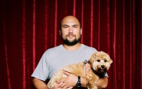 Casually dressed man holding a cute West Highland terrier dog in front of a red velvet curtain