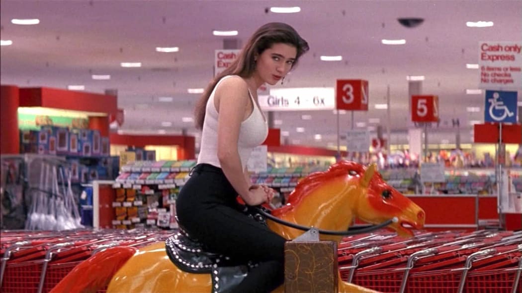 Movie still from the 1991 film Career Opportunities featuring Jennifer Connelly riding a child's coin-operated rocking horse